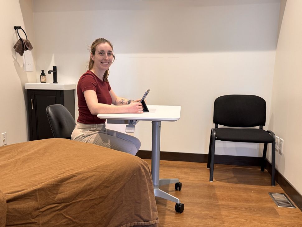a woman sits at a desk with a bed in the foreground